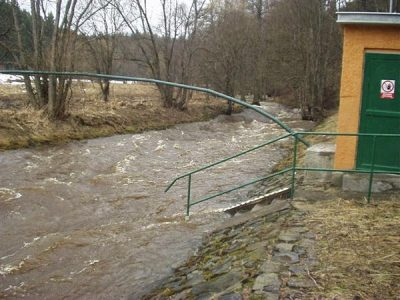Vodočet u měrného objektu Vodočetná lať u měrného objektu na rozvodněném toku se zeleným zábradlím