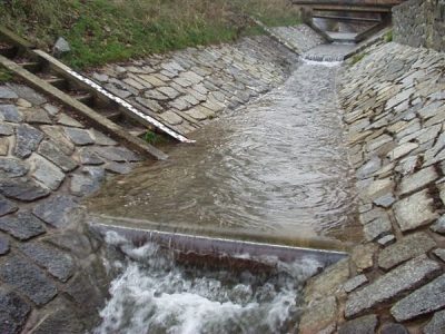 Vodočet v dlážděném korytě Šikmá vodočetná lať kotvená v dlážděném korytě nad přepadovým prahem